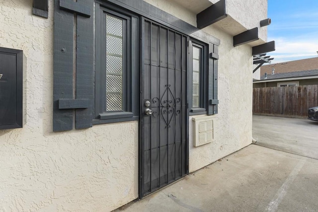 entrance to property featuring visible vents, fence, a patio, and stucco siding