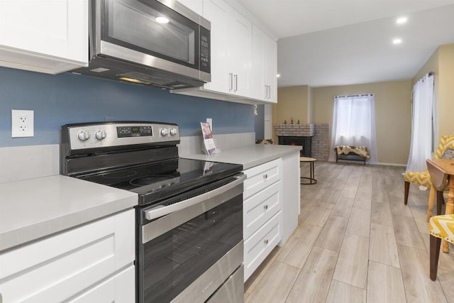 kitchen with stainless steel appliances, light countertops, light wood-style floors, a fireplace, and white cabinetry