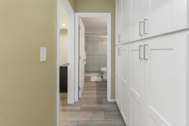 corridor with light wood-type flooring and a textured wall