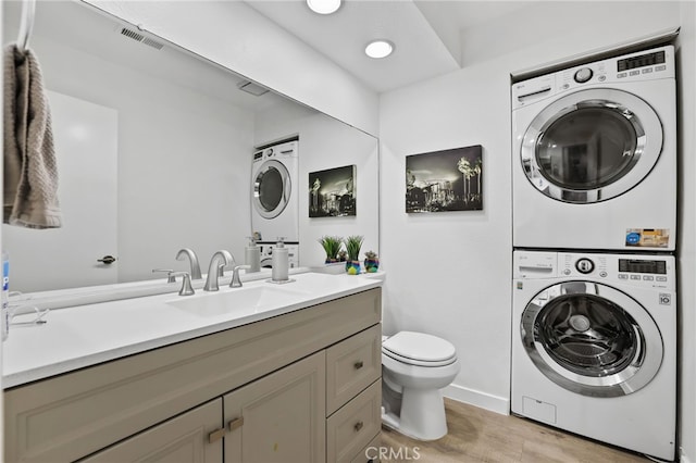 bathroom with toilet, vanity, wood-type flooring, and stacked washer and clothes dryer