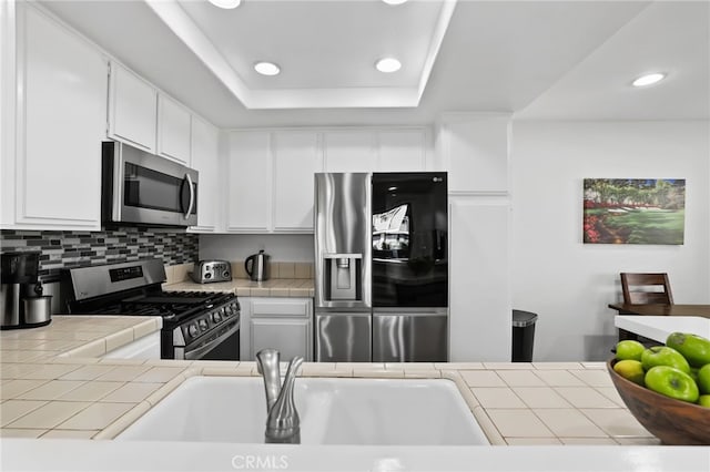 kitchen with tile counters, white cabinets, stainless steel appliances, and a raised ceiling