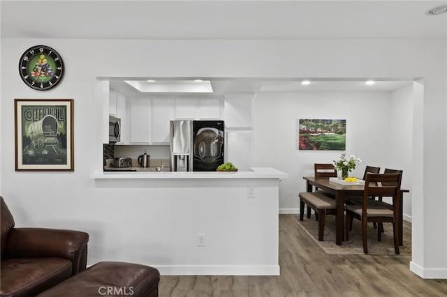 kitchen with light wood-type flooring, kitchen peninsula, appliances with stainless steel finishes, and white cabinetry