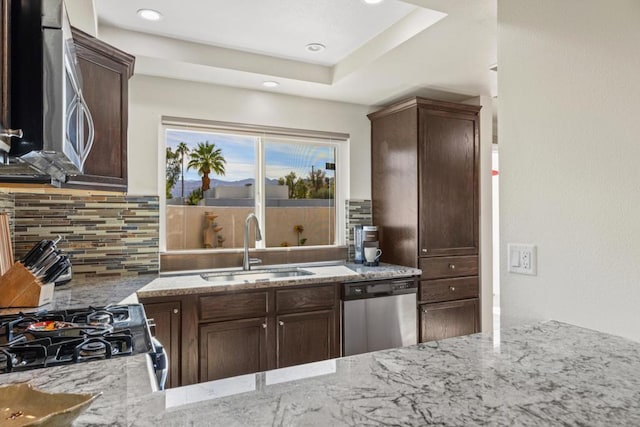 kitchen with light stone countertops, stainless steel appliances, decorative backsplash, sink, and dark brown cabinets