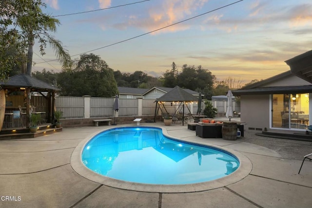 pool at dusk with a diving board, an outdoor living space, a gazebo, and a patio