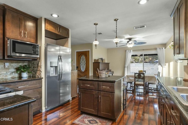 kitchen featuring ceiling fan, a kitchen island, decorative backsplash, stainless steel appliances, and dark hardwood / wood-style flooring