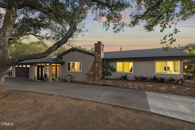 ranch-style home featuring a chimney, an attached garage, board and batten siding, driveway, and roof with shingles
