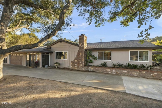 ranch-style home featuring concrete driveway, an attached garage, a chimney, and board and batten siding