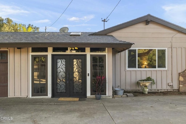 property entrance with board and batten siding, a shingled roof, and french doors