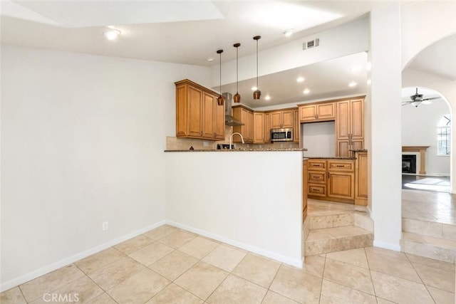 kitchen with pendant lighting, wall chimney exhaust hood, decorative backsplash, ceiling fan, and light tile patterned floors