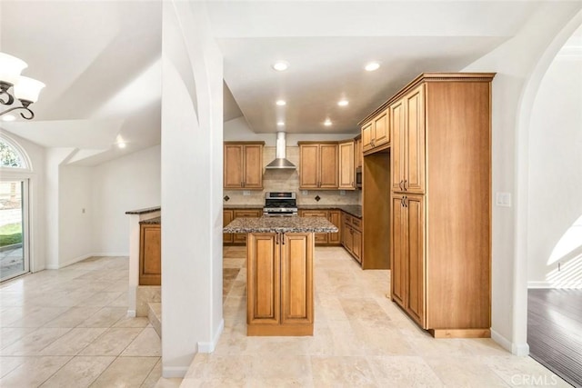 kitchen featuring appliances with stainless steel finishes, decorative backsplash, dark stone countertops, a kitchen island, and wall chimney exhaust hood