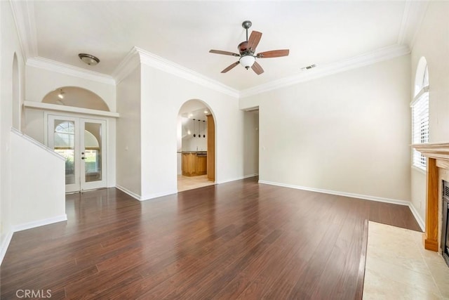 unfurnished living room featuring ceiling fan, crown molding, a tiled fireplace, dark wood-type flooring, and french doors