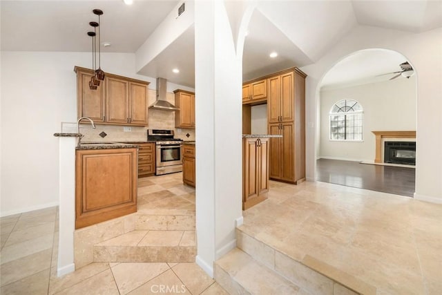 kitchen with lofted ceiling, wall chimney exhaust hood, sink, ceiling fan, and stainless steel range with gas cooktop