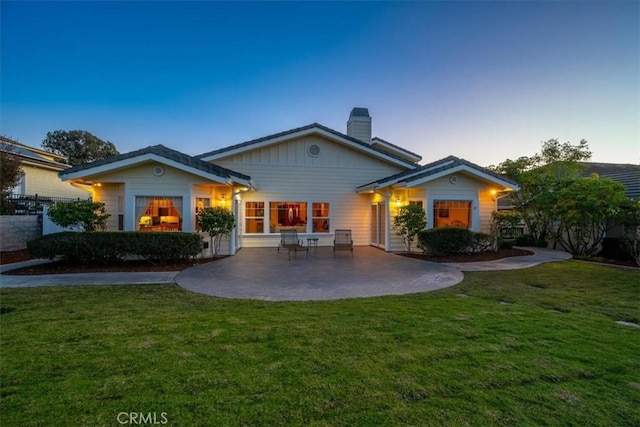 back house at dusk with a lawn and a patio