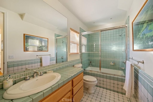 full bathroom featuring shower / bath combination with glass door, vanity, toilet, and tile walls