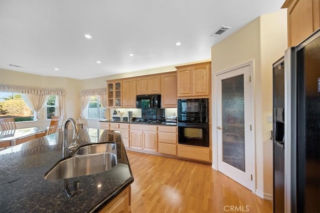 kitchen with dark stone countertops, sink, light hardwood / wood-style flooring, and black appliances