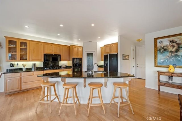 kitchen featuring sink, a kitchen island with sink, light hardwood / wood-style flooring, and black appliances