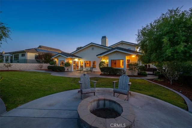 back house at dusk featuring a patio, a yard, and a fire pit