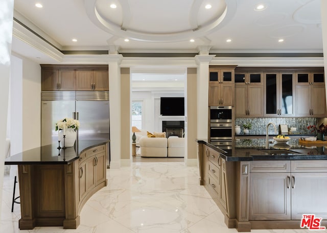 kitchen with appliances with stainless steel finishes, decorative backsplash, a tray ceiling, a large island with sink, and sink