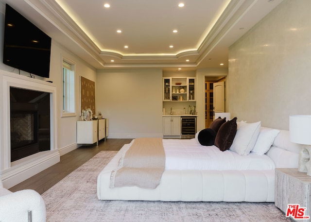 bedroom featuring wood-type flooring, beverage cooler, a tray ceiling, and bar area