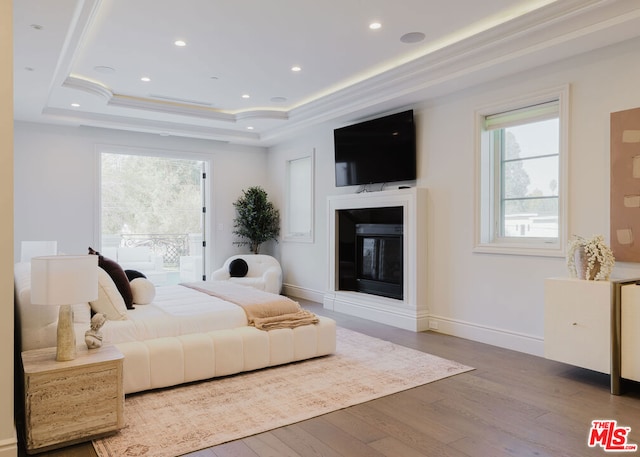 bedroom featuring multiple windows, a tray ceiling, light hardwood / wood-style flooring, and crown molding