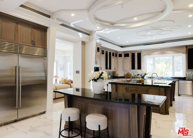 kitchen featuring a large island with sink, decorative backsplash, crown molding, appliances with stainless steel finishes, and a breakfast bar area