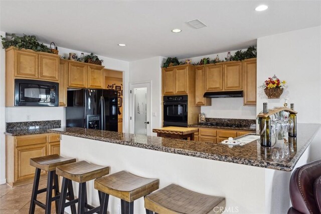 kitchen with black appliances, dark stone counters, a kitchen breakfast bar, kitchen peninsula, and light tile patterned floors