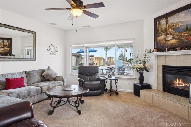 carpeted living room with ceiling fan and a tiled fireplace