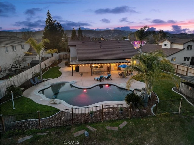 pool at dusk featuring a patio area and a lawn