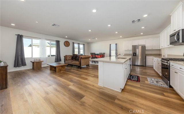 kitchen with light wood-type flooring, stainless steel appliances, white cabinets, and a kitchen island with sink