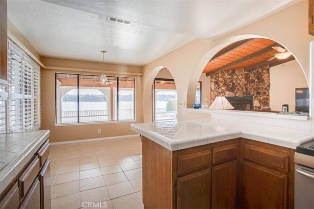 kitchen with light tile patterned flooring, a wealth of natural light, tile counters, and a stone fireplace