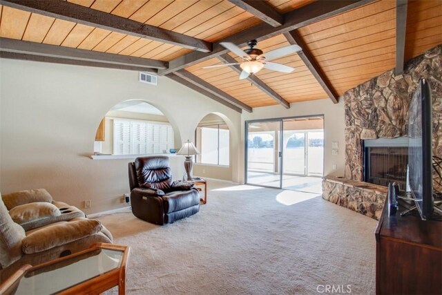 carpeted living room featuring ceiling fan, wood ceiling, a stone fireplace, and lofted ceiling with beams