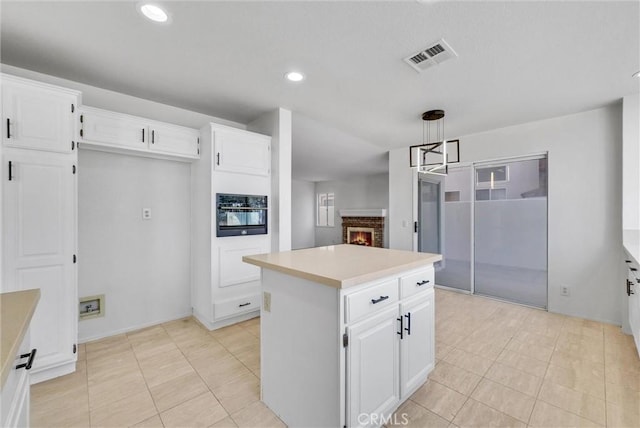 kitchen with pendant lighting, a center island, white cabinetry, oven, and a brick fireplace