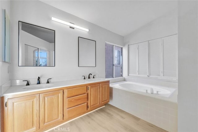 bathroom with vaulted ceiling, tiled tub, wood-type flooring, and vanity