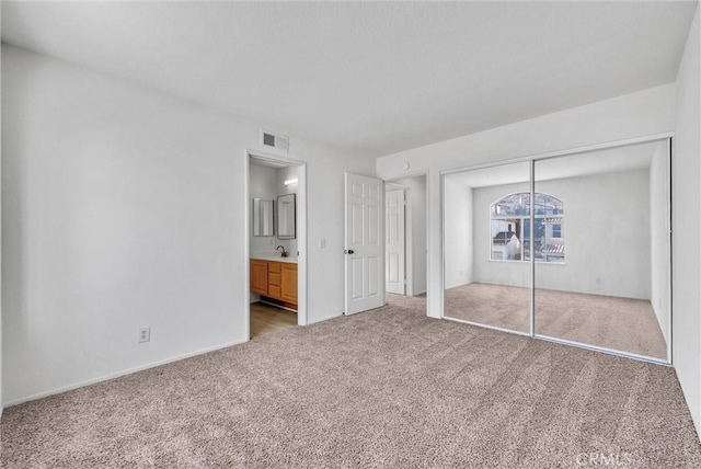 unfurnished bedroom with ensuite bath, light colored carpet, a closet, and sink