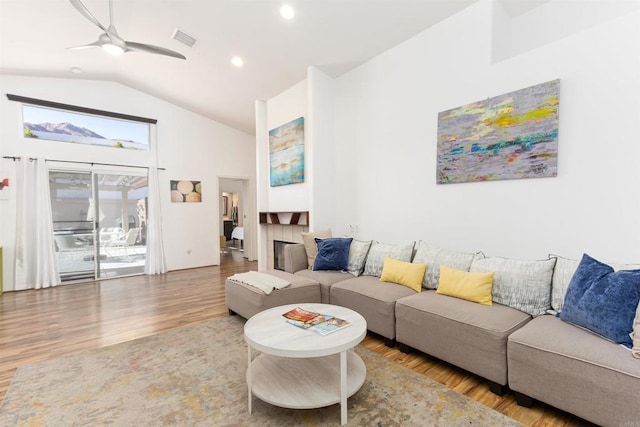 living room featuring wood-type flooring, vaulted ceiling, ceiling fan, and a fireplace