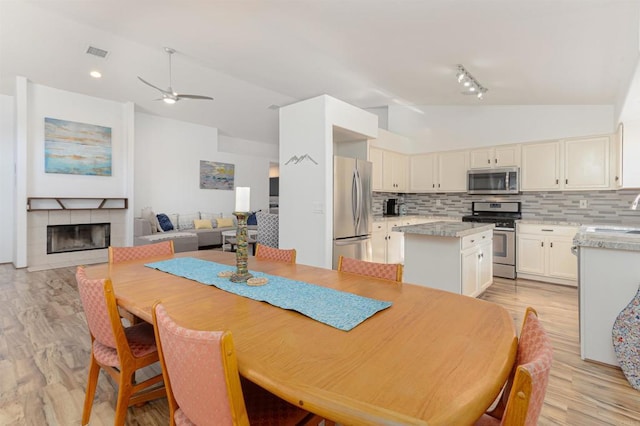 dining space featuring a tile fireplace, high vaulted ceiling, sink, ceiling fan, and light hardwood / wood-style floors