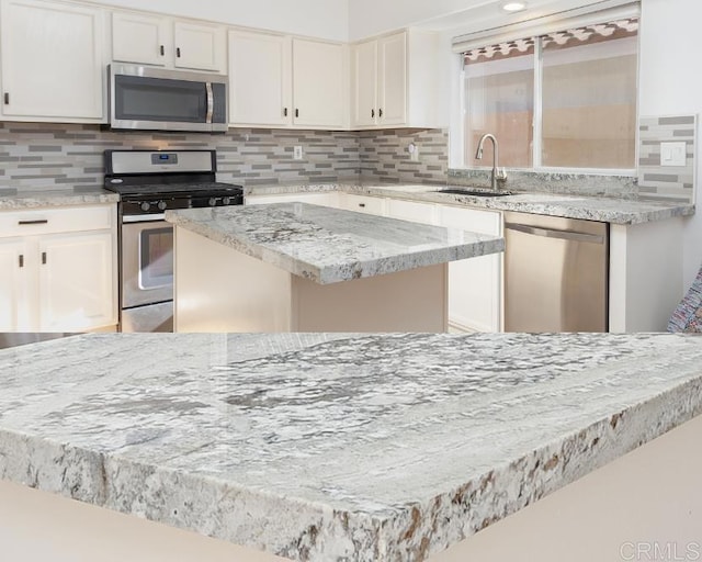 kitchen with sink, white cabinetry, tasteful backsplash, appliances with stainless steel finishes, and a kitchen island