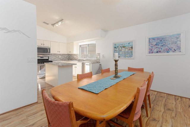 dining room featuring lofted ceiling, rail lighting, visible vents, and light wood-style floors