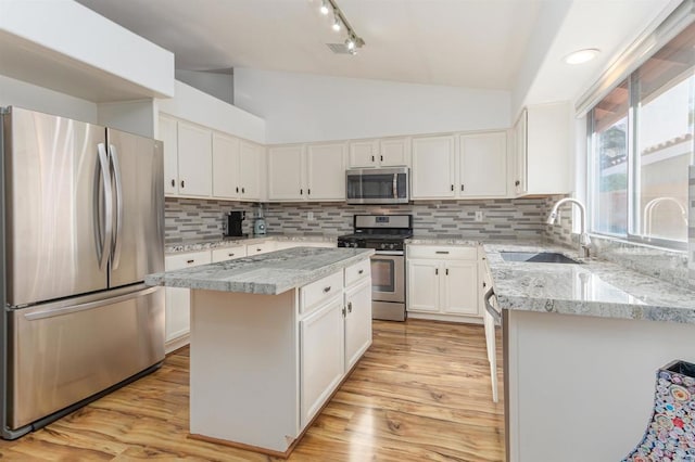 kitchen featuring lofted ceiling, appliances with stainless steel finishes, a sink, a kitchen island, and light wood-type flooring