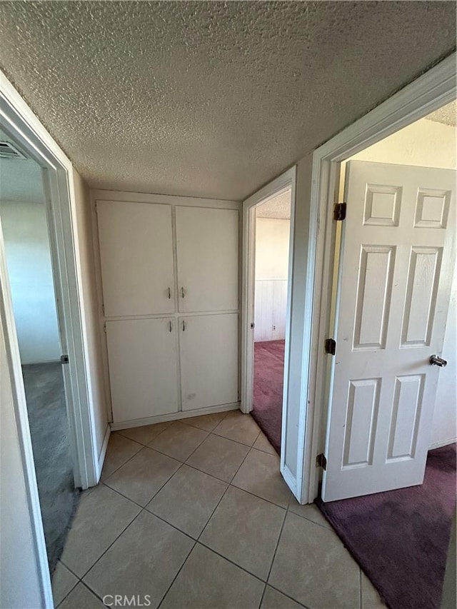 corridor featuring a textured ceiling and light tile patterned floors