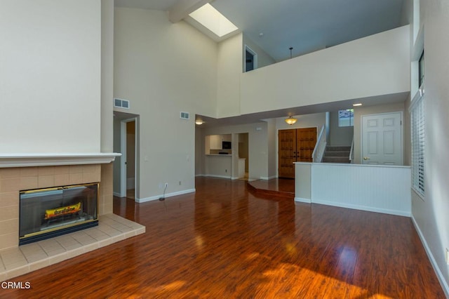 unfurnished living room with beam ceiling, hardwood / wood-style flooring, a tile fireplace, and high vaulted ceiling