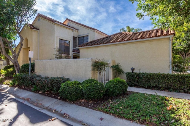 view of side of home with fence, a tile roof, and stucco siding