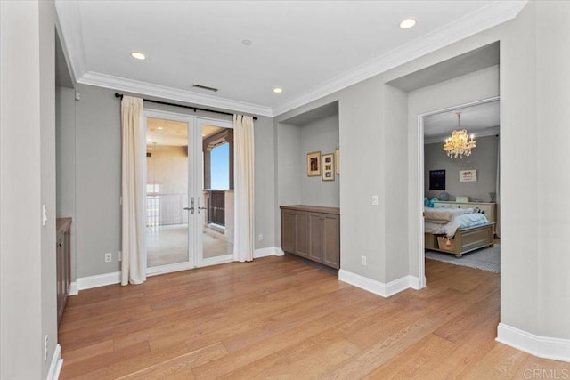 spare room with light wood-type flooring, a chandelier, ornamental molding, and french doors