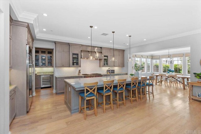 kitchen with hanging light fixtures, wall chimney range hood, crown molding, and a large island