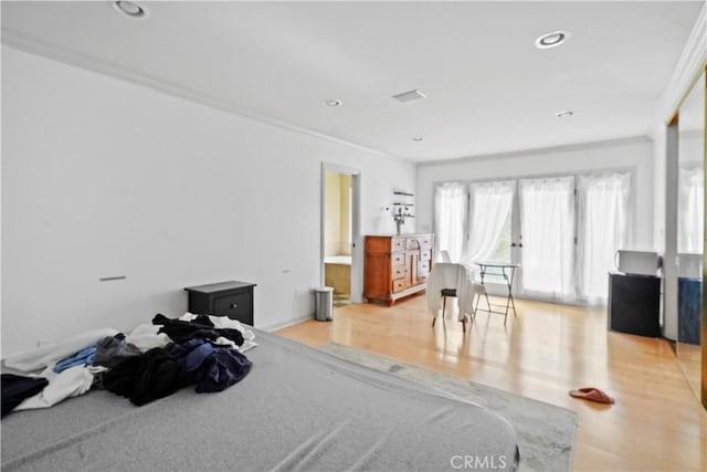 bedroom with light wood-type flooring, ornamental molding, and ensuite bath