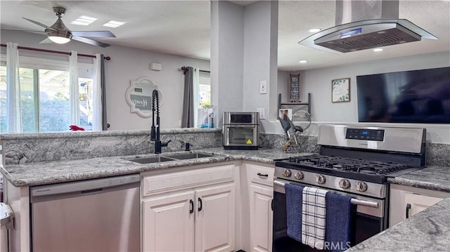 kitchen with appliances with stainless steel finishes, white cabinetry, island exhaust hood, sink, and light stone counters