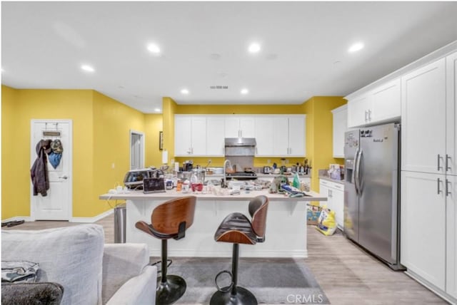 kitchen featuring white cabinetry, stainless steel refrigerator with ice dispenser, a breakfast bar, and a center island with sink