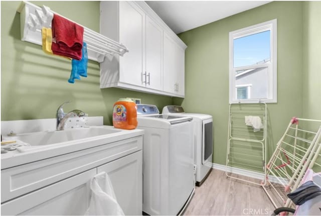 clothes washing area with cabinets, washing machine and clothes dryer, and light hardwood / wood-style flooring