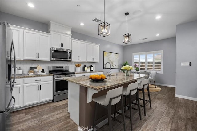 kitchen featuring stone counters, pendant lighting, white cabinetry, a kitchen island with sink, and appliances with stainless steel finishes