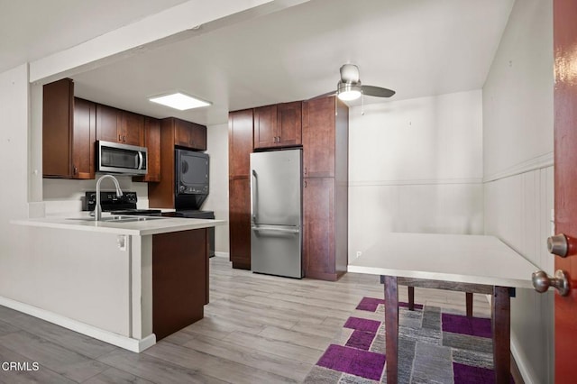 kitchen featuring stacked washer and dryer, kitchen peninsula, ceiling fan, stainless steel appliances, and sink